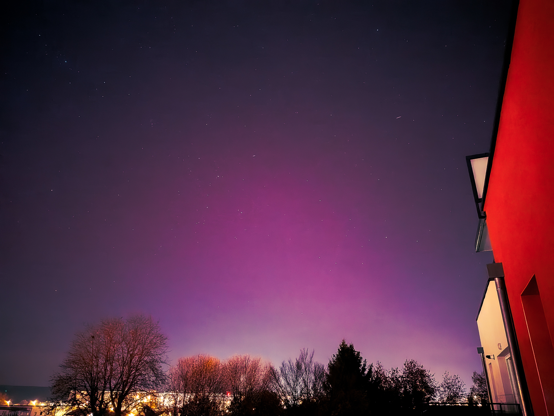 Pink and violet aurora over a town skyline